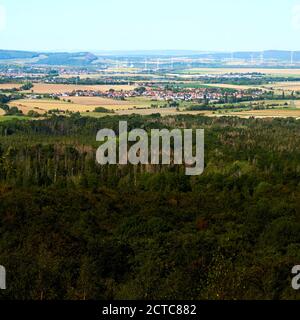 View over the dense green forest in the Harz Mountains to a village near Bad Harzburg with wind turbines in the background Stock Photo