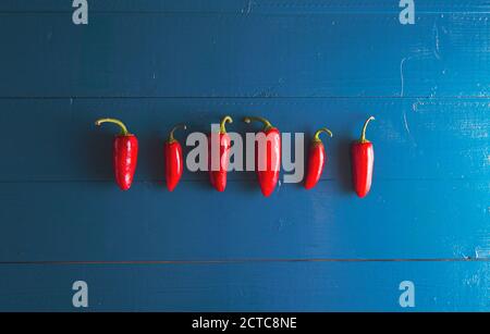 Minimal flat lay view of chili peppers in a row over blue vintage backdrop with copy space Stock Photo