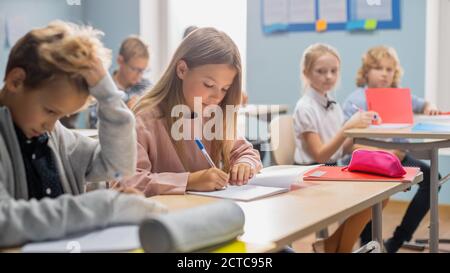 Elementary Classroom of Diverse Children Listening Attentively to their Teacher Giving Lesson. Brilliant Young Kids in School Writing in Exercise Stock Photo