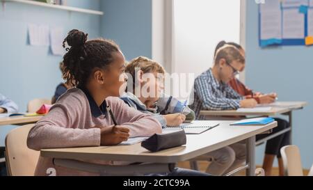 Elementary Classroom of Diverse Bright Children Listening Attentively to their Teacher Giving Lesson. Brilliant Young Kids in School Learning to Be Stock Photo