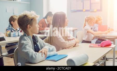 Elementary Classroom of Diverse Bright Children Listening Attentively to their Teacher Giving Lesson. Brilliant Young Kids in School Learning to Be Stock Photo