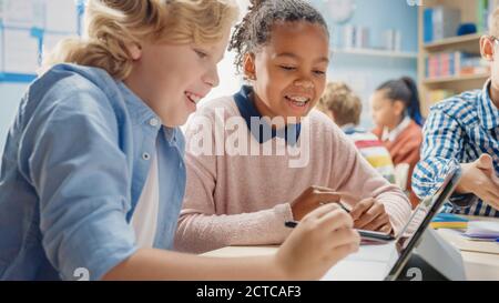 In the Elementary School: Girl and a Boy Work as a Team Using Tablet Computers, Learning Programming Language, Internet Safety and Robotics Design Stock Photo