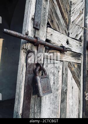 An metal large rusty padlock is hanging on the wooden doors Stock Photo