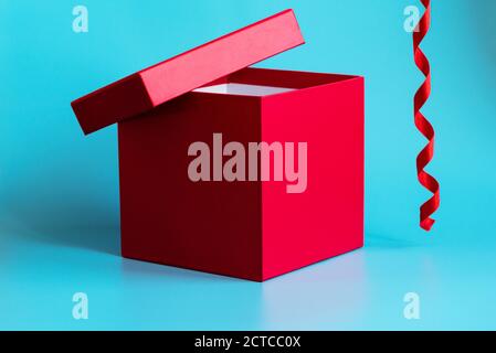 Red gift box with lid ajar and spiral ribbon on light blue background. Closeup. Holidays concept. Mockup for greeting or advertising Stock Photo