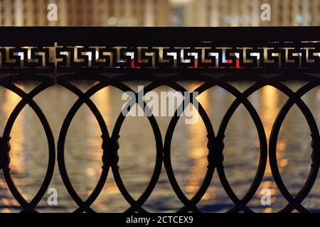 View of Moskva river, city reflections at the water through the metal fence. Concept of the beauty of the Moscow city in night. Buildings across the r Stock Photo