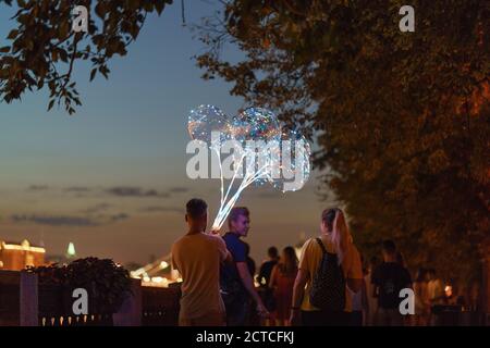 Moscow, Russia - July 6, 2020: People  walking in the Gorky park. Youth playing with big glowing balloons. City architecture as defocused background. Stock Photo