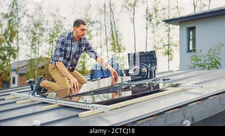 Caucasian Man in Checkered Shirt is Installing Black Reflective Solar Panels on a Metal Basis. He Works on a House Roof on a Sunny Day. Concept of Stock Photo