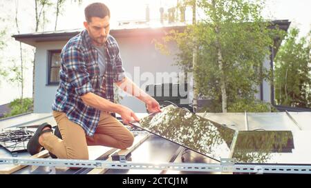 Caucasian Man in Checkered Shirt is Installing Black Reflective Solar Panels on a Metal Basis. He Works on a House Roof on a Sunny Day. Concept of Stock Photo