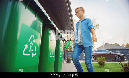 Young Boy is Walking Outside His Home in Order to Throw Away Two Empty Plastic Bottles into a Trash Bin. He Uses Correct Garbage Bin Because This Stock Photo