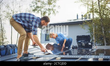 Father and Son Installing Solar Panels to a Metal Basis. They are Holding the Panels on a House Roof on a Sunny Day. Concept of Ecological Renewable Stock Photo