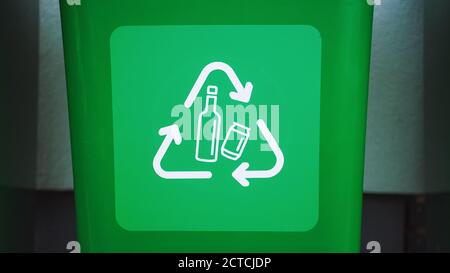 Close-up Shot of a Green colored, plastic garbage bin, with bottle recycle logos on front. Concept of waste sorting for bottles. Saving Environment Stock Photo