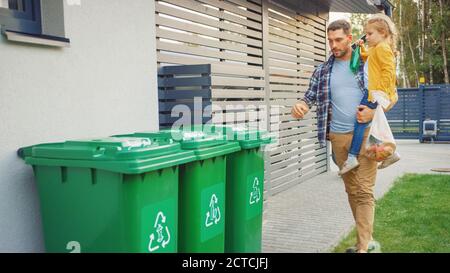 Father Holding a Young Girl and Going to Throw Away an Empty Bottle and Food Waste into the Trash. They Use Correct Garbage Bins Because This Family Stock Photo