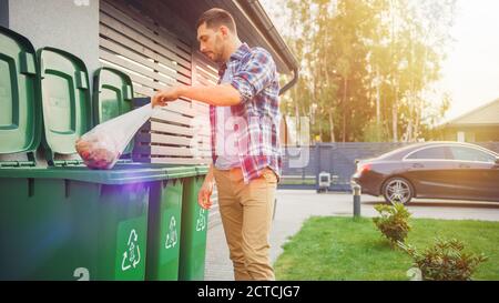 Caucasian Man is Throwing Away Two Plastic Bags of Trash next to His House. One Garbage Bag is Sorted with Biological Food Waste, Other with Stock Photo