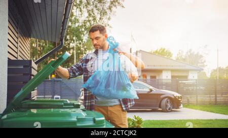 Caucasian Man is Throwing Away Two Plastic Bags of Trash next to His House. One Garbage Bag is Sorted with Biological Food Waste, Other with Stock Photo