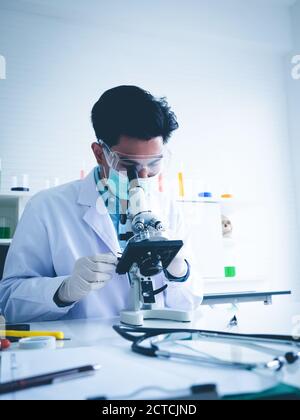 Asian male scientist Is working seriously Chemistry experiment With looking at the microscope In the laboratory, the color tone image. Stock Photo