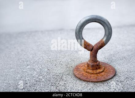 Rusty eye loop or loop screw. Close up. Bolted to an outdoor cement tile covering the patio drain. Eye loops are used to attach ropes or cables. Stock Photo