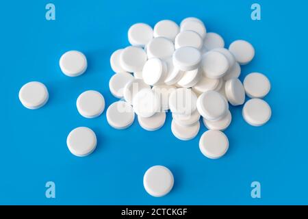 Pile of white pills on light blue background. Many disc shaped tablets. Chalky and not coated. No imprints. Drug abuse concept Stock Photo