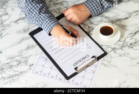 Man writing checklist next to cup of coffee on office table top view Stock Photo