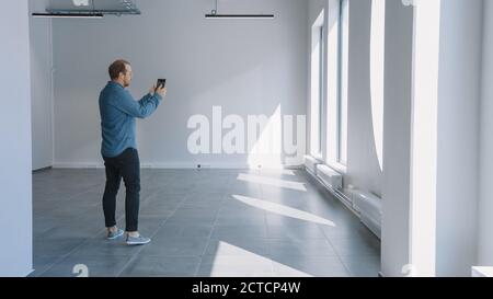 Young Hipster Man in Jeans Shirt Standing in Empty Office and Map it with an Augmented Reality Software on a Tablet. Sunlight Shines Through Big Stock Photo