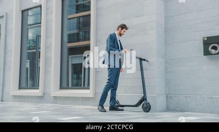 Businessman in a Suit is Activating an Electric Scooter with a Smartphone. He's Scaning the QR Code. Modern Entrepreneur Uses Contemporary Ecological Stock Photo