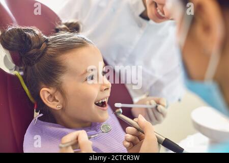 Brave little girl getting tooth cavity from dentist and assistant in dental clinic Stock Photo