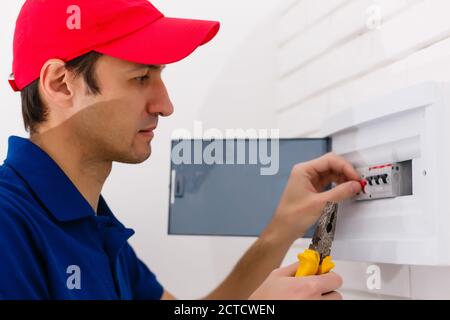 Young adult electrician builder engineer screwing equipment in fuse box Stock Photo
