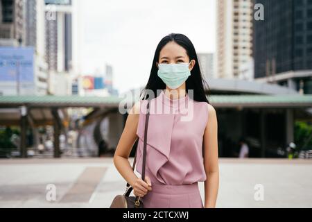 Asian businesswoman wearing protective Covid face covering facing camera, urban setting, city life, pandemic Stock Photo