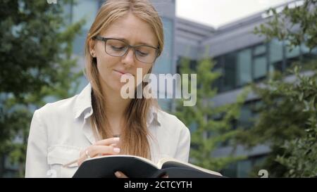 Thoughtful young woman making notes in her note pad and looking Stock Photo