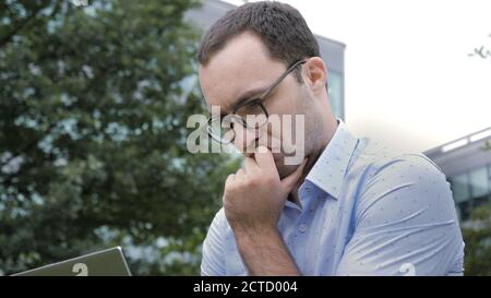 Handsome young businessman using a laptop sitting thinking and r Stock Photo