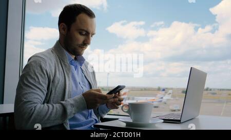 Businessman checking his phone while working on a laptop at the Stock Photo