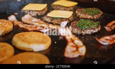 Tasty Shot of a Meat Patties Being Prepared. Fresh Ground Beef is Grilled on a Hot Gas or Electric Grill. Cook is Adding Cheese Slices on Top of Stock Photo