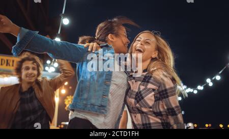 Group of Friends are Having a Party Outside a Street Food Burger Cafe. Two Beautiful Girls Hugging and Dancing to Music. It's Evening in a Modern Stock Photo
