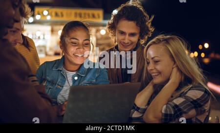 Beautiful and Handsome Friends are Using a Laptop Computer while Standing at a Table in an Outdoors Street Food Cafe. They're Watching a Video or an Stock Photo