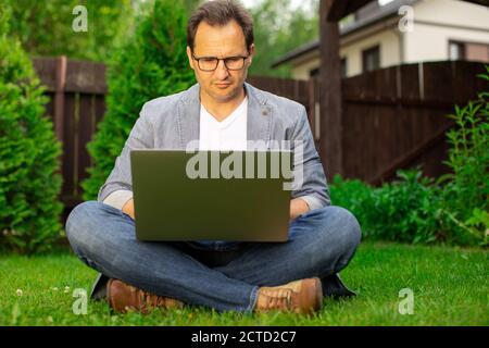 Middle aged businessman working on laptop outdoors, checking stock market Stock Photo