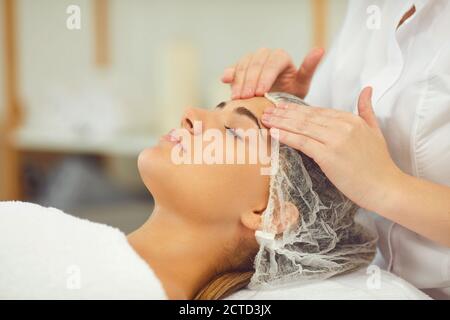 Woman getting procedure of relaxing facial massage treatment from cosmetologist Stock Photo