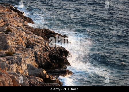 Waves break on rocks on the seashore with white splashes. Blue foamy water on a stones, sea background Stock Photo