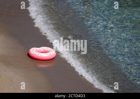 Inflatable ring in donut shape on a sand in sea waves, aerial view. Background for beach vacation, relax and leisure in clean water Stock Photo