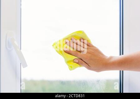 Washing a window pane with a yellow microfiber cloth, close-up with a blurred background. Autumn or spring cleaning concept. Stock Photo