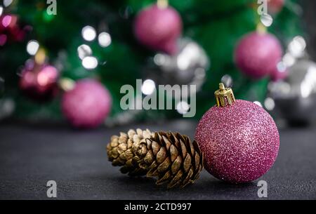 Purple bauble and golden colored pine cone on blurred Christmas lights background. Close up, copy space Stock Photo
