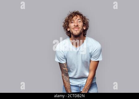 Freestyle. Man with curly hair standing isolated on grey leaning towards camera joyful Stock Photo
