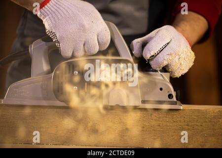 woodworker making wooden detail and using electric plane throws sawdust Stock Photo
