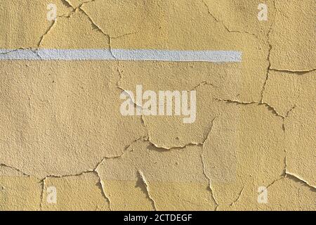 Old cracked weathered painted wall background texture. Yellow color wall with white line. Stock Photo