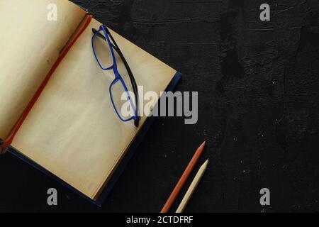 Blank opened advertising folder isolated on black background. With reading glasses and pencils. Stock Photo