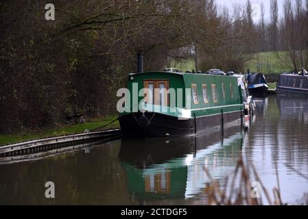 A green canal boat is reflected in still water in this photo taken along the Grand Union canal in Buckinghamshire Stock Photo