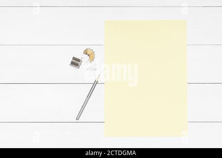 a pencil, a pencil sharpener and a yellow sheet of paper on a white wooden table Stock Photo