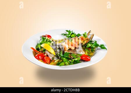 The head of the fish, mussels, greens and prawns are on a white plate. Restaurant service. The plate is floating in the air Stock Photo
