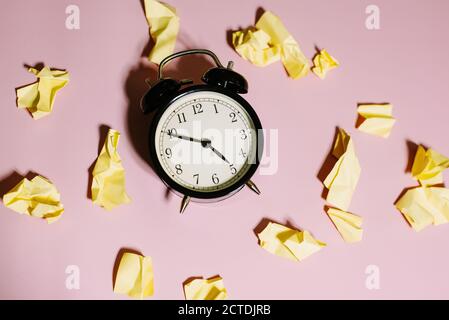 The concept of deadlines and the generation of ideas. Top view of classic alarm clock with crumpled yellow sticky notes on pink background. Stock Photo