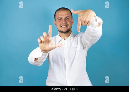 Russian business man wearing white shirt standing over blue background doing frame using hands palms and fingers, camera perspective Stock Photo