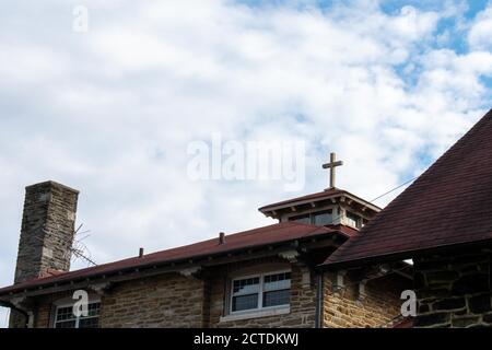 A Cross on the Red Roof of a Cobblestone Convent With a Cloudy Blue Sky Behind It Stock Photo
