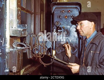 Hump master in a Chicago and Northwestern [i.e. North Western] railroad yard operating a signal switch system which extends the length of the hump track. He is thus able to control movements of locomotives pushing the train over the hump from his post at the hump office; Chicago, Ill. December 1942 Stock Photo